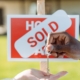 Someone giving a house key to someone behind 'house sold' sign